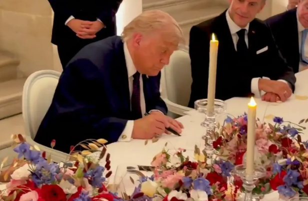 President Trump signs a copy of the US-Iran memorandum of understanding by hand over dinner with French President Macron